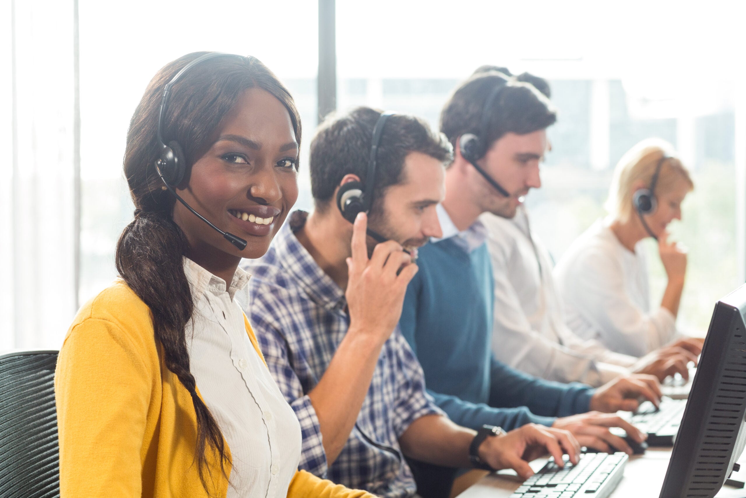 Team working on computer with headset while a colleague smiling at camera in the office